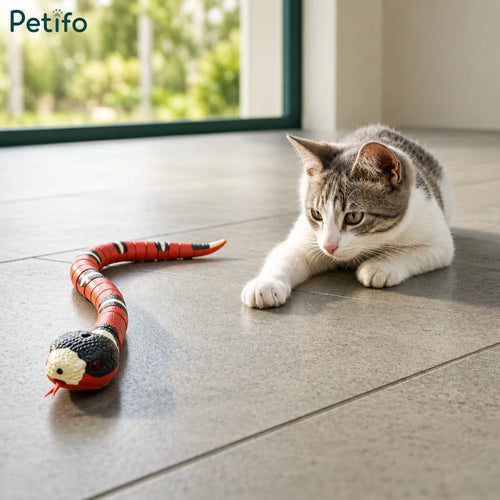 Cute tabby kitten playing with an interactive electronic snake toy on a tiled floor.