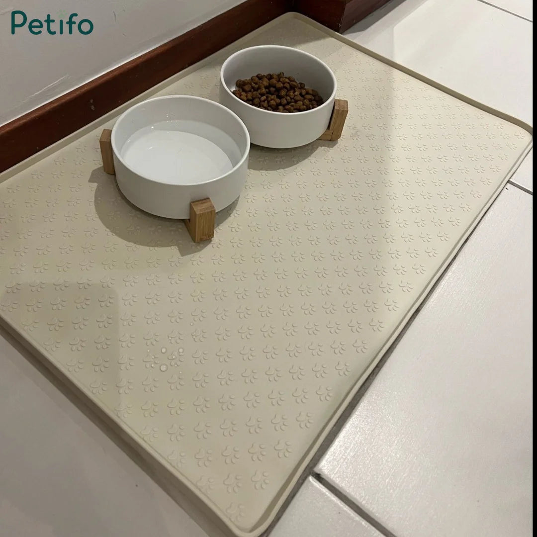 Beige pet silicone mat holding two white bowls with wooden stands containing food and water on a tiled floor.