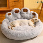 A dog sleeping soundly in a plush gray paw bed with brown paw pads on a wooden floor.